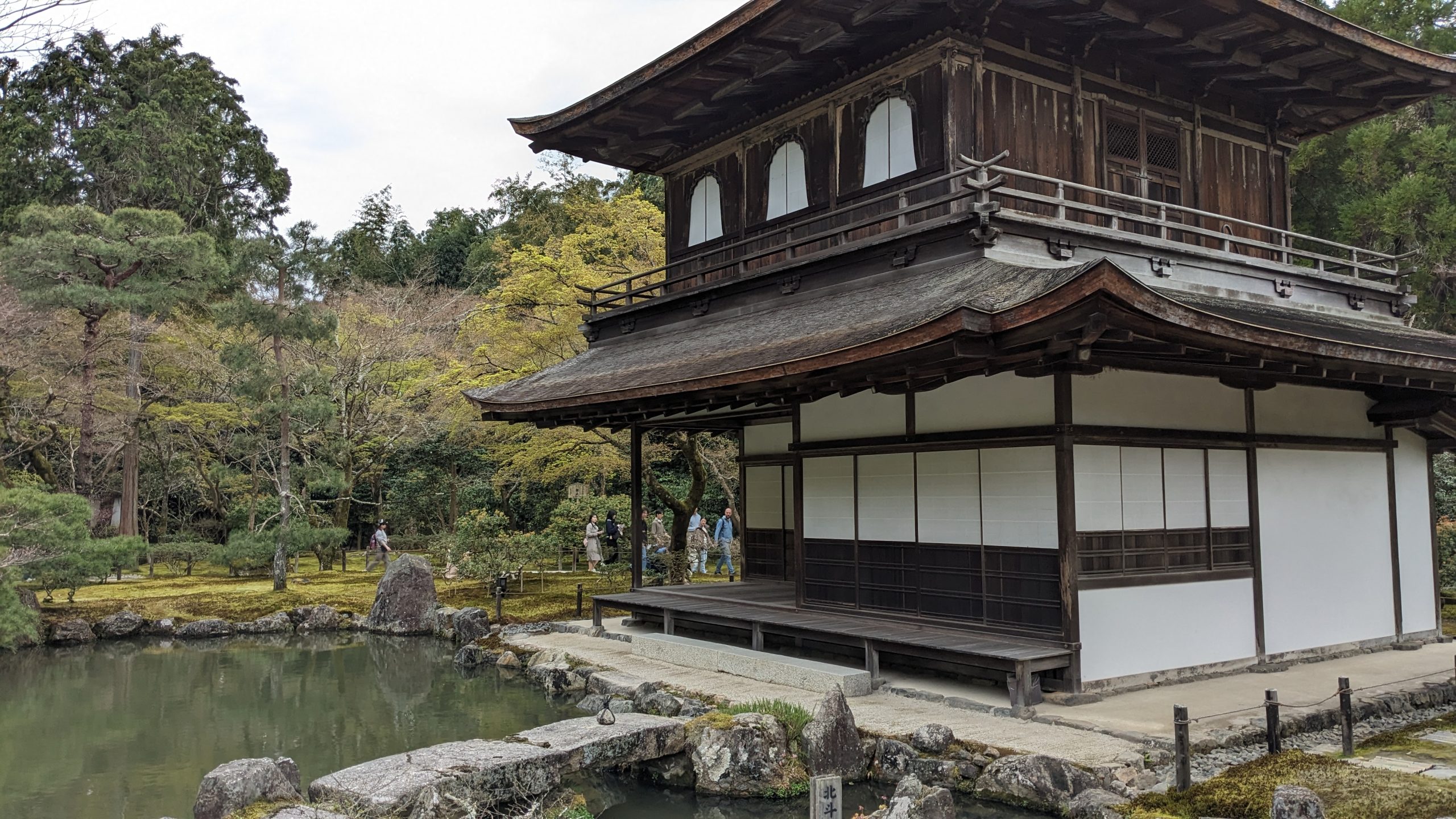 Tempio zen Ginkaku-Ji a due piani con struttura in legno scuro e pareti bianche, situato a Kyoto, Giappone, accanto a uno stagno tranquillo circondato da alberi verdi e muschio nel giardino tradizionale giapponese